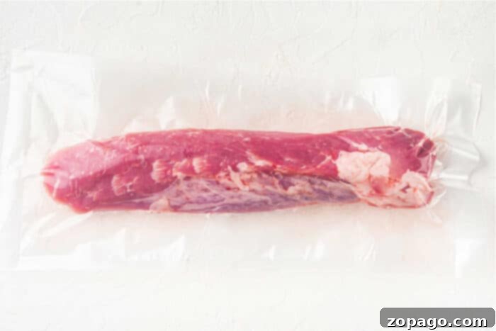 Succulent Pork Tenderloin Tacos 3 A vacuum-sealed package containing a raw, whole pork tenderloin on a plain, light-colored surface. The meat is pink with visible marbling and fat along its side—perfect for making mouthwatering Pork Tenderloin Tacos.