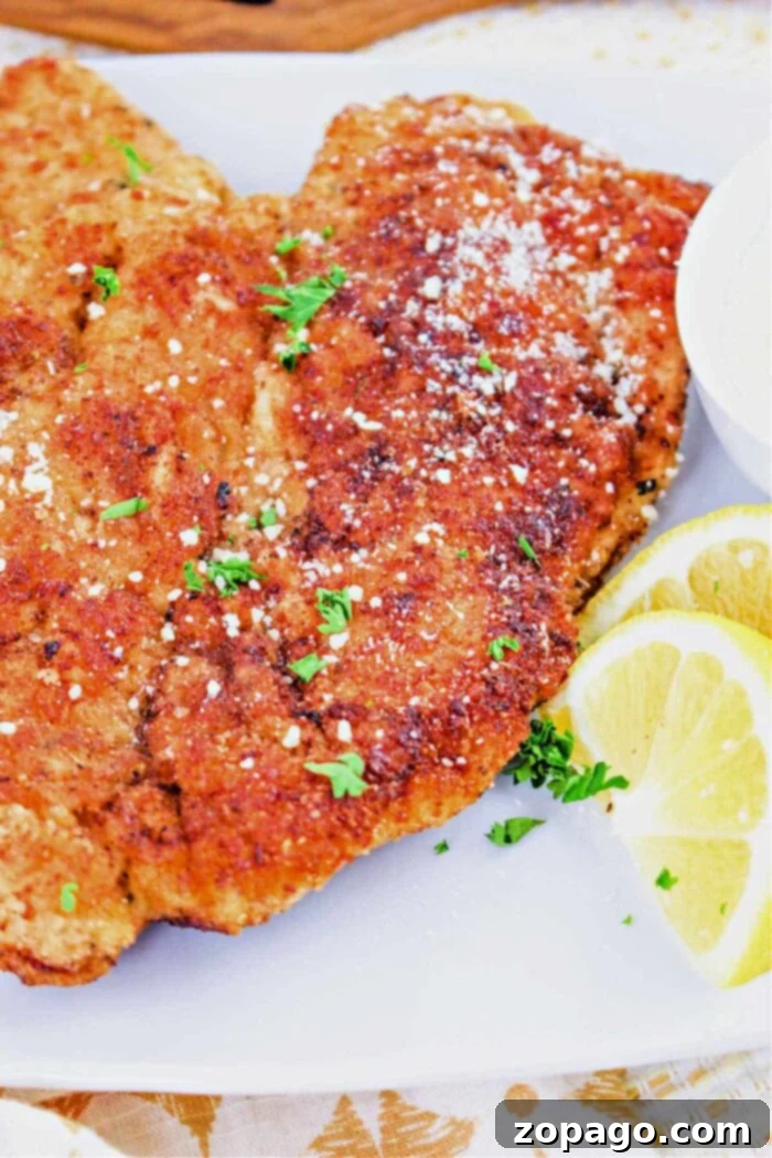 Perfectly Baked Chicken Cutlets 2 A close-up of breaded baked chicken cutlets whose perfect timing is essential, garnished with fresh herbs and served alongside zesty lemon slices on a pristine white plate.