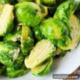 A close-up of beautifully boiled Brussels sprouts, seasoned with fresh herbs and a sprinkle of crumbled cheese, elegantly presented on a white plate. They are cooked to the perfect tender-crisp texture, demonstrating that knowing how long to boil Brussels sprouts significantly enhances their flavor and appeal, making every bite a delight.