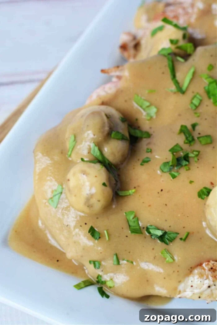 Tender Pork Chops Smothered in Rich Mushroom Gravy 7 A hearty plate of pork chops with creamy mushroom sauce, elegantly garnished with chopped fresh parsley, ready to enjoy.