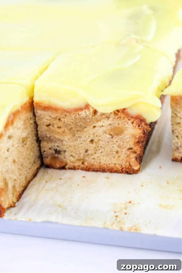 Everyday Banana Cake 2 A close-up of a Banana snack Cake, featuring a sliced cake topped with creamy yellow frosting on a white surface.
