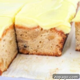 A slice of Banana Cream Cake with visible nuts sits enticingly on a white surface, its frosted layers promising a delightful taste adventure.