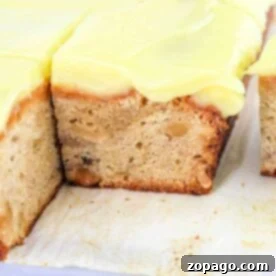 Everyday Banana Cake 6 A slice of Banana Cream Cake with visible nuts sits enticingly on a white surface, its frosted layers promising a delightful taste adventure.