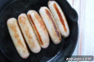 Five brats cooking in a cast iron skillet, with golden brown grill marks on each—these Crockpot Brats can also be slow-cooked for even more juicy flavor.