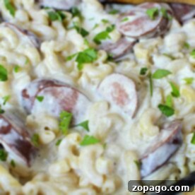 Creamy macaroni with sliced kielbasa and parsley in a skillet, stirred with a wooden spoon—a delightful pasta recipe thats both hearty and satisfying.