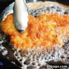 Golden Fried Chicken Perfection 8 Tongs holding a golden-brown fried chicken cutlet sizzling in hot oil.