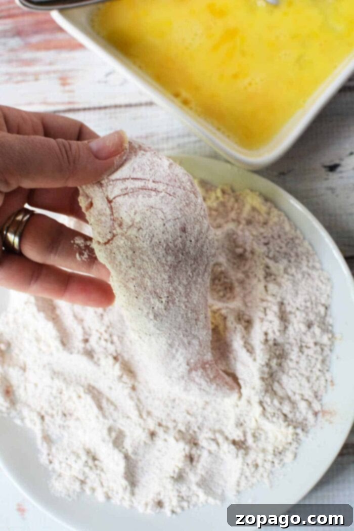 Mastering Crispy Homemade Chicken Tenders 3 Hand dipping chicken fillet in flour, with beaten eggs nearby, this process mirrors the initial steps of learning how to make chicken tenders.