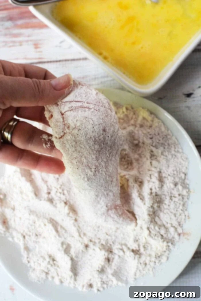 Crispy Homemade Chicken Tenders 3 Hand dipping chicken fillet in flour, with beaten eggs nearby, this process mirrors the initial steps of learning how to make chicken tenders.