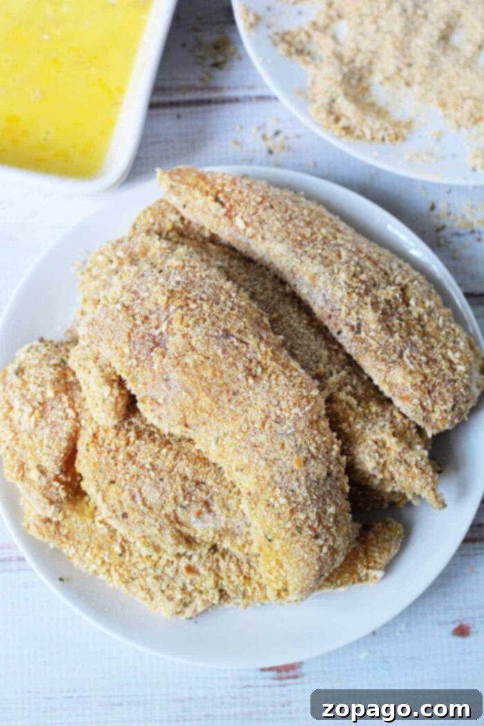 Mastering Crispy Homemade Chicken Tenders 6 A white plate showcases crispy breaded chicken fillets, while in the backdrop, you can see all the essentials for creating your own masterpiece. This setup might just inspire your next cooking adventure after learning how to make chicken tenders at home.