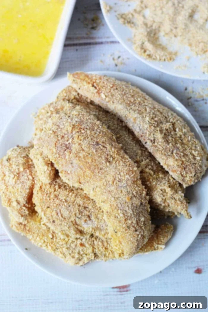 Crispy Homemade Chicken Tenders 6 A white plate showcases crispy breaded chicken fillets, while in the backdrop, you can see all the essentials for creating your own masterpiece. This setup might just inspire your next cooking adventure after learning how to make chicken tenders at home.