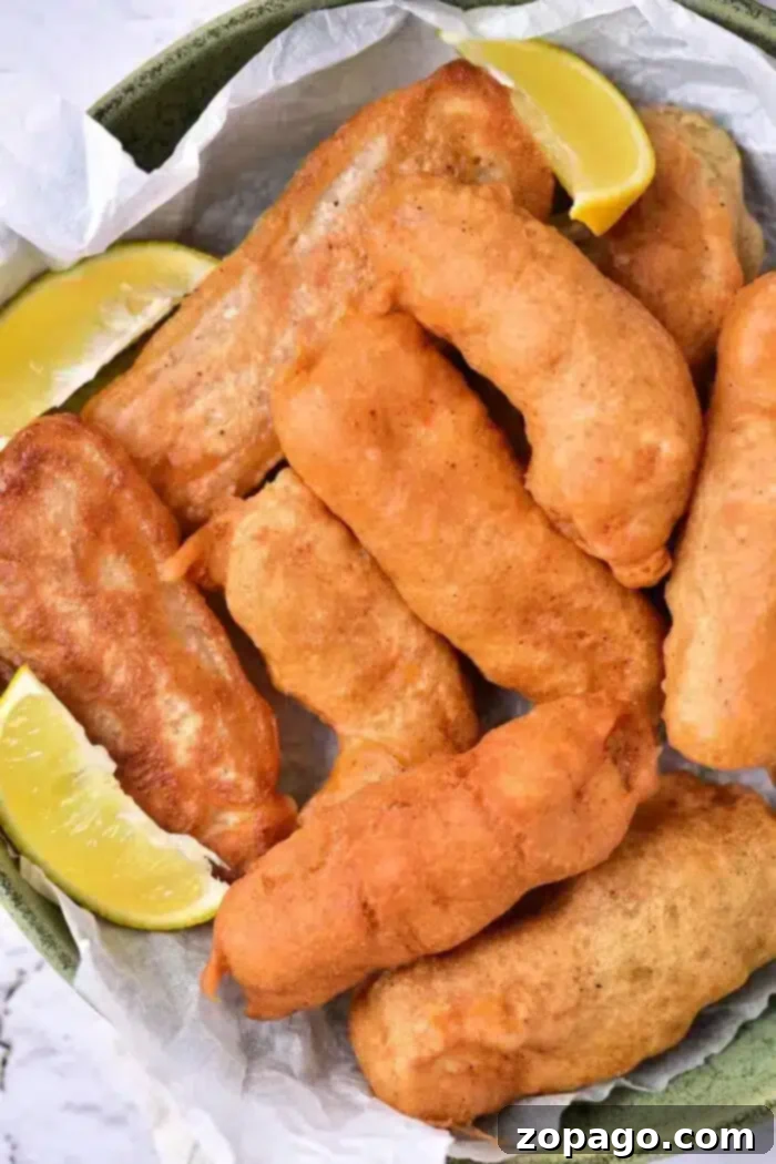Secrets to Crispy Beer Batter 2 A plate of golden-brown beer-battered fish pieces is arranged on parchment paper in a bowl. Two lemon wedges are placed alongside the fish, adding a zesty contrast to the savory delight.