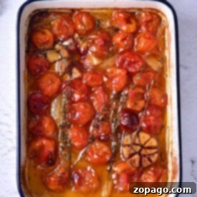 Tomato Confit Recipe: Succulent roasted cherry tomatoes and garlic in a rectangular baking dish, enhanced with aromatic herbs on a light surface.