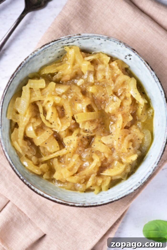 Sweet Caramelized Onion Confit 6 A bowl of glossy, golden-brown onion confit rests on a rustic beige napkin. The soft texture and slight seasoning of black pepper are visible, with cutlery subtly blurred in the background, hinting at a meal.