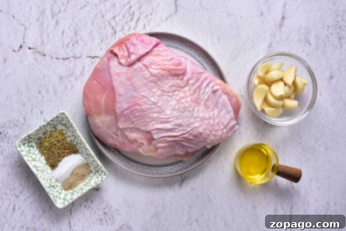 Slow Cooked Turkey Breast Confit 3 A raw turkey breast on a plate is placed on a kitchen countertop. Surrounding it are a small dish of spices, including salt and pepper, a bowl with peeled garlic cloves, and a small container of olive oil—perfect ingredients for preparing Turkey Confit.