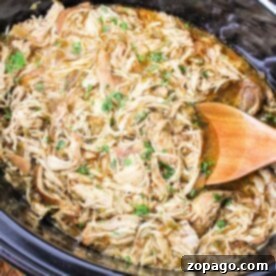 Crockpot Green Chili Chicken simmers gently as shredded chicken blends with herbs.