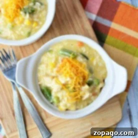 A bowl of creamy chicken and vegetables, crafted from leftover chicken breast, is topped with shredded cheese and sits invitingly on a wooden board alongside gleaming forks.