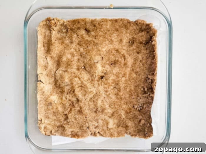 Easy Peach Crumble Bars 5 Buttery shortbread crust, golden and inviting, ready to cradle a luscious peach filling, baked to perfection in a pristine square pan.