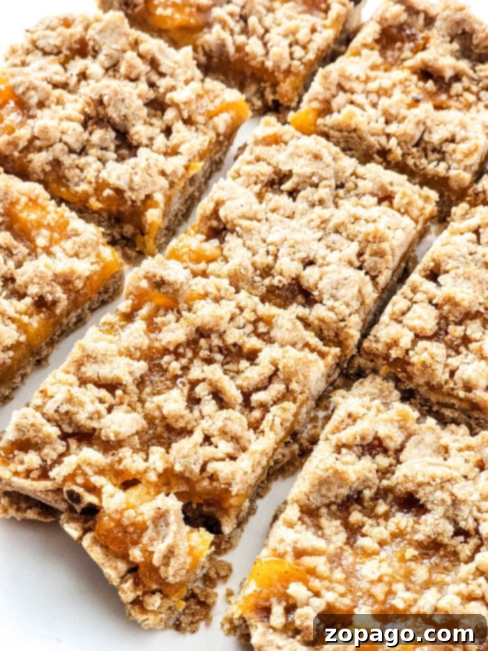 Easy Peach Crumble Bars 8 A close-up view of beautifully baked peach bars, showcasing a rich, golden streusel topping and a vibrant, bubbling peach filling, ready to be enjoyed.