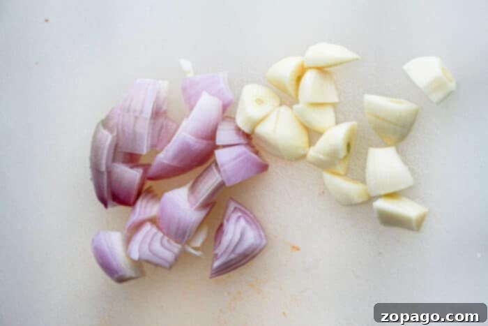 Fiery Garlic Chili Paste 3 Chopped pieces of red onions and garlic cloves are arranged on a white cutting board. The red onion pieces are on the left, and the garlic pieces, key ingredients for a Garlic Chili Paste Recipe, are on the right.