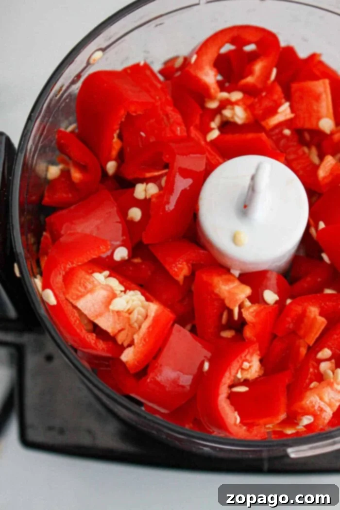 Homemade Fiery Chili Garlic Paste 5 A food processor bowl filled with coarsely chopped red bell peppers, visible seeds, and hints of garlic, ready for blending into a delicious chili paste recipe.
