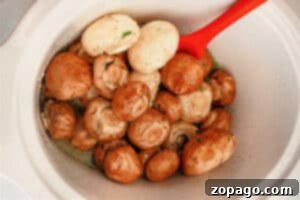 Crockpot mushrooms seasoned with a fragrant herb and garlic blend, resting in a white slow cooker.
