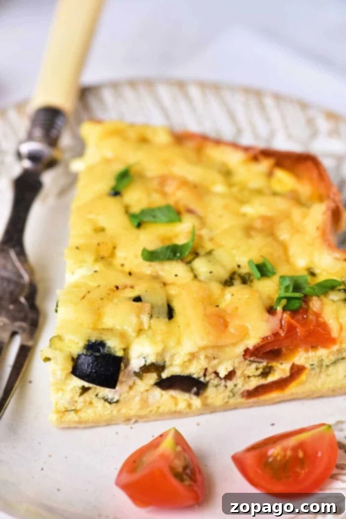 Creamy Cottage Cheese Quiche 7 A vibrant slice of vegetable cottage cheese quiche on a plate, featuring zucchini, tomato, melted cheese, and green onions. A decorative fork and cherry tomato halves complete the presentation.