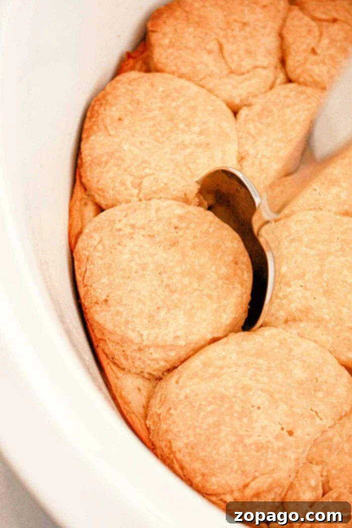 Slow Cooker Biscuits and Gravy. There is a silver spoon resting on top of one of the golden brown biscuits. The biscuits are arranged close together in the dish.