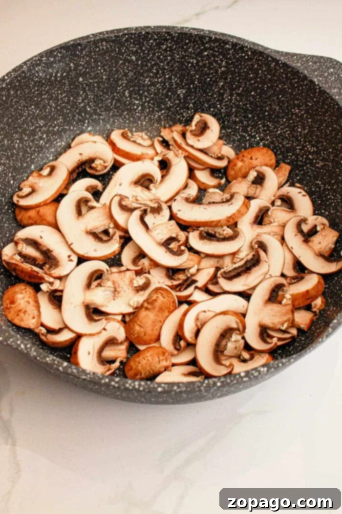A black, speckled frying pan filled with slices of raw mushrooms sits invitingly on a light-colored countertop, setting the perfect stage for a hearty Slow Cooker Biscuits and Gravy breakfast.