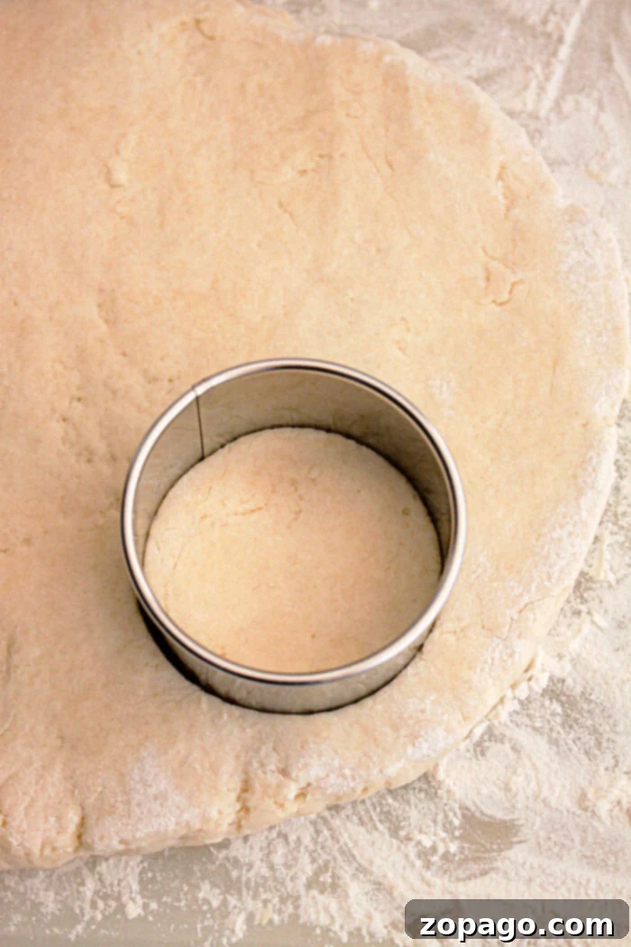 A metal round cookie cutter is pressed into rolled-out dough on a floured surface, creating a perfect shape for Slow Cooker Biscuits and Gravy.
