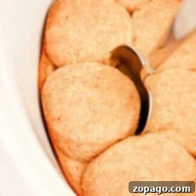 Slow Cooker Biscuits and Gravy. There is a silver spoon resting on top of one of the golden brown biscuits. The biscuits are arranged close together in the dish.