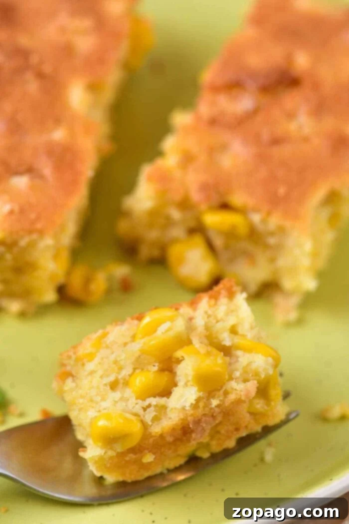 Homemade Creamy Corn Pudding 5 A close-up view of a generous piece of corn casserole, visibly rich with corn kernels, presented on a vibrant green plate. A fork in the foreground holds a smaller bite, highlighting the dish's irresistible texture, characteristic of a homemade corn pudding without Jiffy mix.