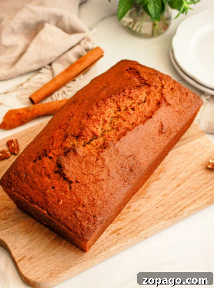 Spiced Sweet Potato Loaf 7 A loaf of freshly baked sweet potato bread with cake mix sits on a wooden cutting board. A cinnamon stick and some whole pecans are visible in the background, alongside a folded beige cloth and a stack of white plates.