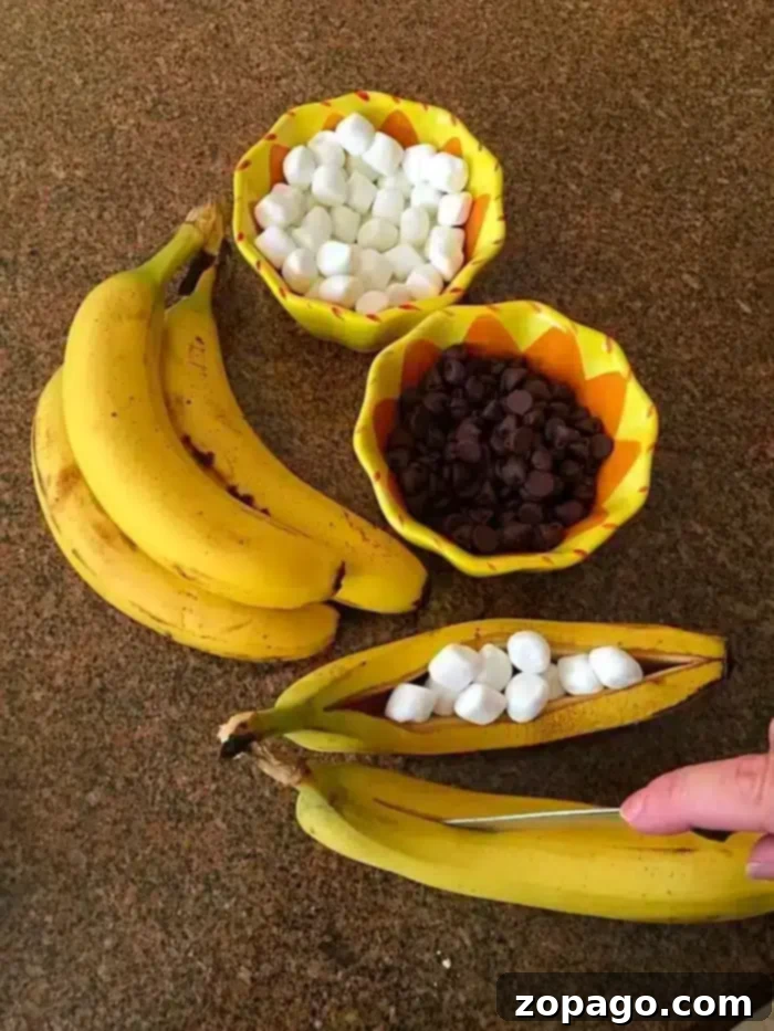 This is the best dessert to prepare on your bbq, banana s'mores! So easy to do and they are served inside the banana skins themselves. Just throw them on and use bananas instead of graham crackers to make this unique smore dessert on the barbecue for the summertime or really all year long. #banana #smores #barbecue #dessert A bunch of bananas sits on a countertop beside two bowls: one filled with mini marshmallows and the other with chocolate chips. A hand cuts open a banana, turning it into a delightful banana s'mores treat by stuffing it with mini marshmallows.