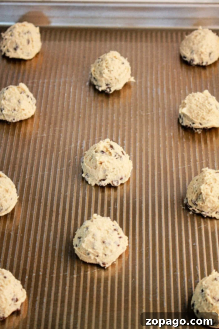 Pancake Mix Cookie Hack 4 Neatly scooped balls of chocolate chip cookie dough, made from pancake mix, are spaced out on a baking sheet lined with parchment paper, perfectly ready for the oven. Visible chocolate chips promise a delightful treat.