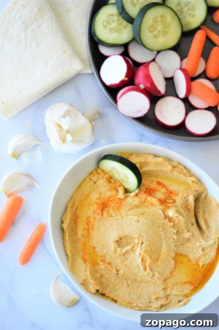 Effortless Hummus: Canned Chickpea Edition 6 A rustic bowl of homemade hummus, garnished with olive oil and paprika, surrounded by fresh vegetables and pita bread.