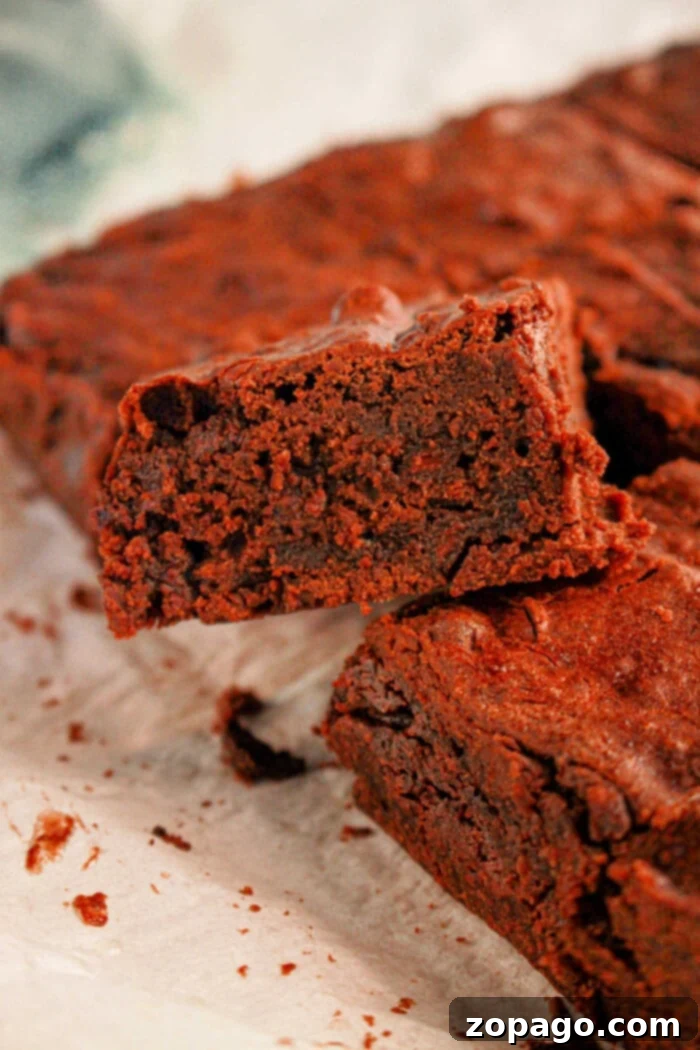 Secretly Fudgy Black Bean Brownies 6 Close-up of a single rich, fudgy black bean brownie on parchment paper, perfectly showcasing its dense and moist texture. The brownie is dark, indicating a deep chocolate flavor.