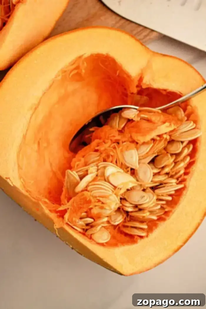 Crockpot Pumpkin Bliss 3 A close-up view of a halved pumpkin with vibrant orange flesh. A spoon is actively scooping out seeds and fibrous strands, illustrating the essential first step in preparing a pumpkin for slow cooking.