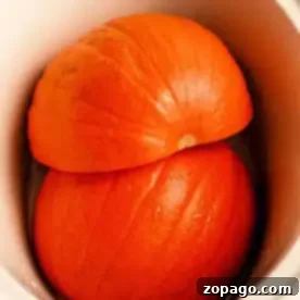 Two large, bright orange pumpkin halves resting snugly inside a white slow cooker, ready for cooking.