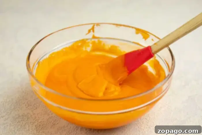 Pumpkin Surprise Loaf Cake 3 A clear glass bowl holds a smooth, vibrant orange cake batter, ready for baking. A red and wooden spatula rests partially covered in the mixture inside the bowl, which is placed on a light-colored, subtly textured countertop, highlighting the rich color of the batter.