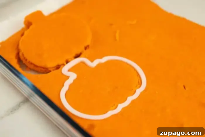 Pumpkin Surprise Loaf Cake 5 A vibrant orange cake slice is shown with a pumpkin-shaped cookie cutter partially pressed into it, creating the outline of a shape. Beside the cutter, a perfectly formed pumpkin cut-out sits ready. The scene, set on a clean white countertop, captures the playful and precise process of creating charming shapes for a surprise inside cake.