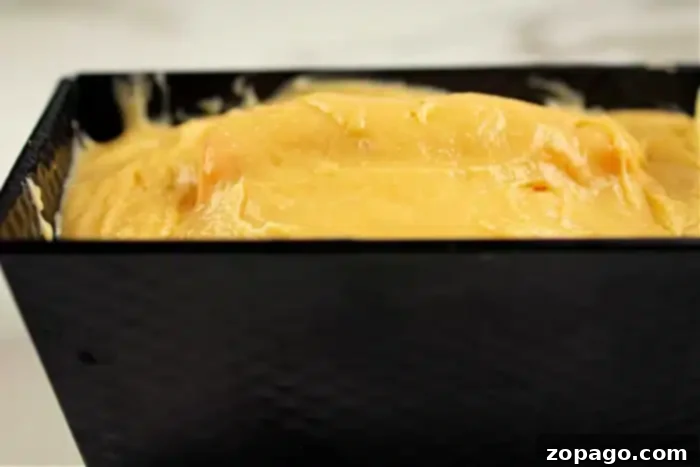Pumpkin Surprise Loaf Cake 6 A close-up shot of thick, smooth yellow cake batter meticulously poured into a rectangular black baking pan. The batter fills the pan almost to the brim, signifying it's ready for baking. This image hints at the delicious, hidden shape soon to be revealed inside the finished cake.