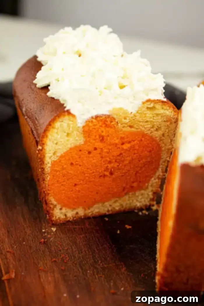 Pumpkin Surprise Loaf Cake 7 A perfectly sliced pound cake rests on a white plate, showcasing a captivating circular orange pumpkin filling within each slice. The top of this delightful surprise cake is generously adorned with a smooth layer of white frosting. The cake is positioned on a rustic wooden cutting board, ready to be enjoyed.