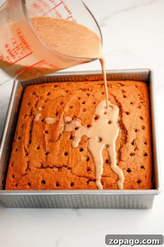 Spiced Pumpkin Poke Cake 4 A square Pumpkin Poke Cake in a metal baking pan is being drizzled with a light brown liquid from a measuring cup. The cake has multiple holes poked into its surface to allow the liquid to seep in, ensuring every bite is moist and flavorful.