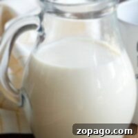A clear glass pitcher filled with creamer sits gracefully on a wooden table, paired with a white and yellow cloth nearby, ready to transform into homemade coffee creamer for your morning brew.