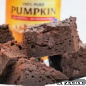 Close-up of 3 ingredient pumpkin brownies stacked in front of a can of pure pumpkin puree. The moist and fudgy treats contrast beautifully with the yellow can's red label in the backdrop.
