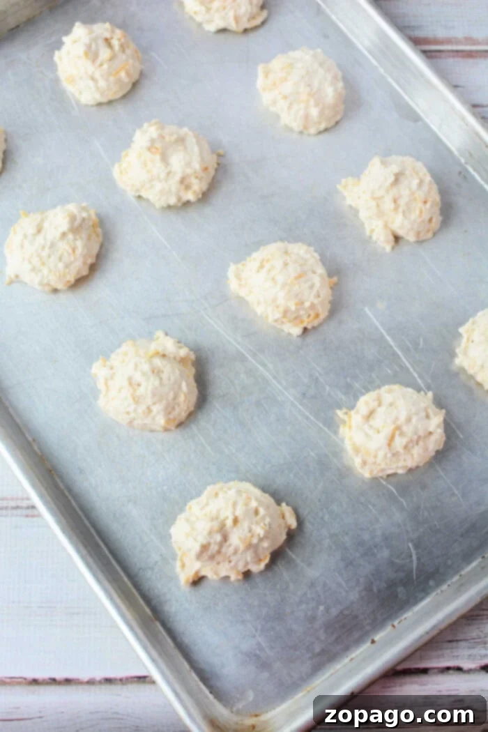 Easy Cheesy Jiffy Biscuits 6 Dollops of Jiffy Mix biscuit dough spaced on a metal baking sheet.