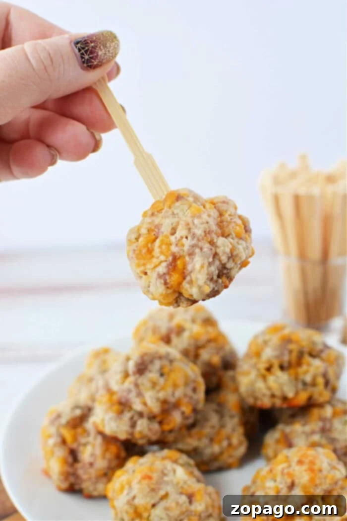 Red Lobster Biscuit Sausage Poppers 6 A hand holds a wooden pick with a delectable cheese and sausage ball, perfectly crafted using Red Lobster Biscuit Mix, above a plate filled with more savory creations, highlighting the golden-brown exterior and cheesy interior.