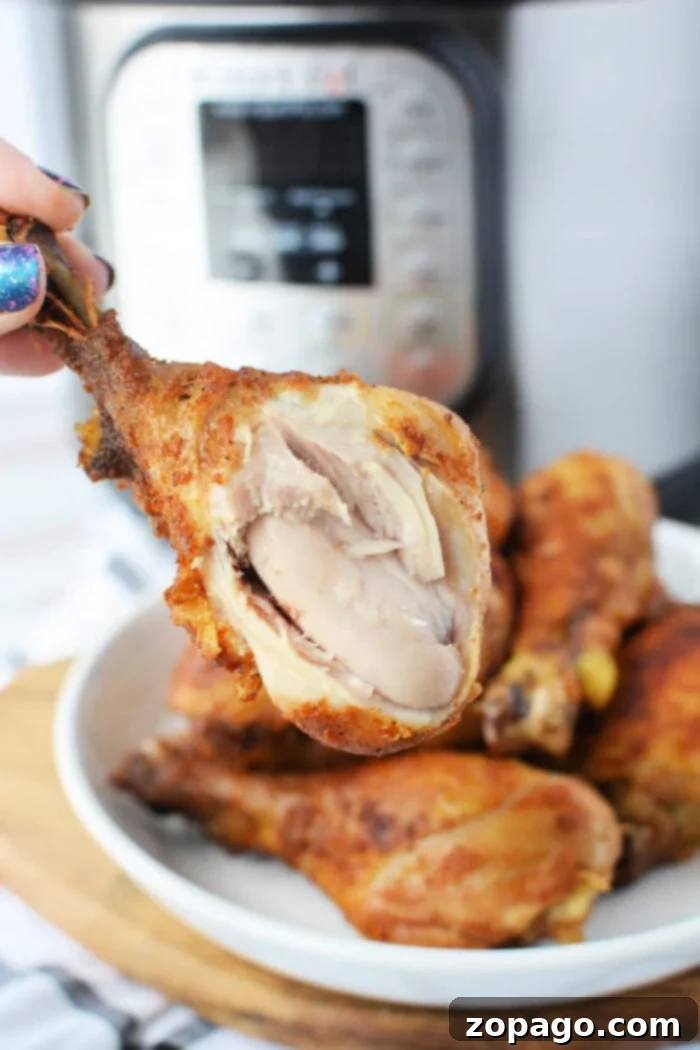 Crispy Pressure Cooker Fried Chicken 2 Close-up of a hand holding a juicy piece of pressure cooker fried chicken with visible meat, set against the backdrop of a gleaming pressure cooker.