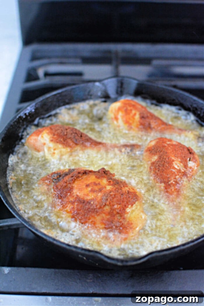 Crispy Pressure Cooker Fried Chicken 5 Four pieces of breaded chicken sizzling in a pan, reminiscent of pressure cooker fried chicken, frying to golden perfection with oil on a stovetop.