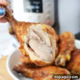 Speedy Pressure Fried Chicken 6 Close-up of a hand holding a juicy piece of pressure cooker fried chicken with visible meat, set against the backdrop of a gleaming pressure cooker.